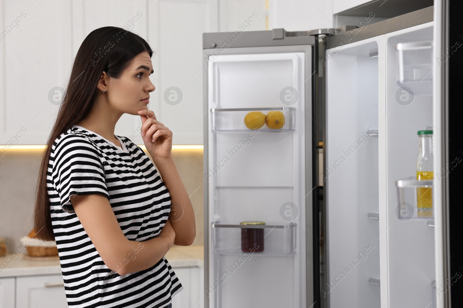 Photo of Upset woman near empty refrigerator in kitchen