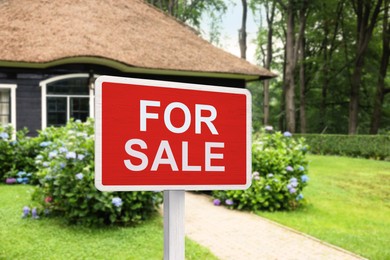 Image of Sale sign near beautiful house outdoors. Red signboard with words