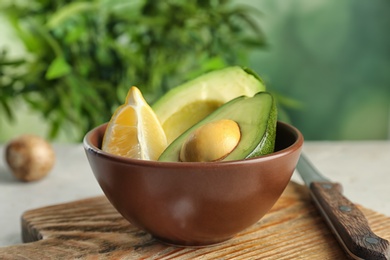 Photo of Bowl with ripe avocado and lemon on wooden board