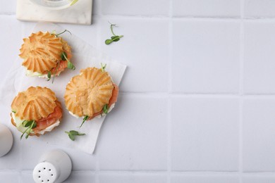 Delicious profiteroles with cream cheese and salmon on white tiled table, flat lay. Space for text