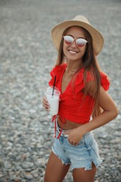 Beautiful young woman with tasty milk shake on beach