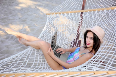 Young woman with laptop resting in hammock at seaside. Summer vacation