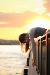 Photo of Young woman leaning over railing outdoors at sunset