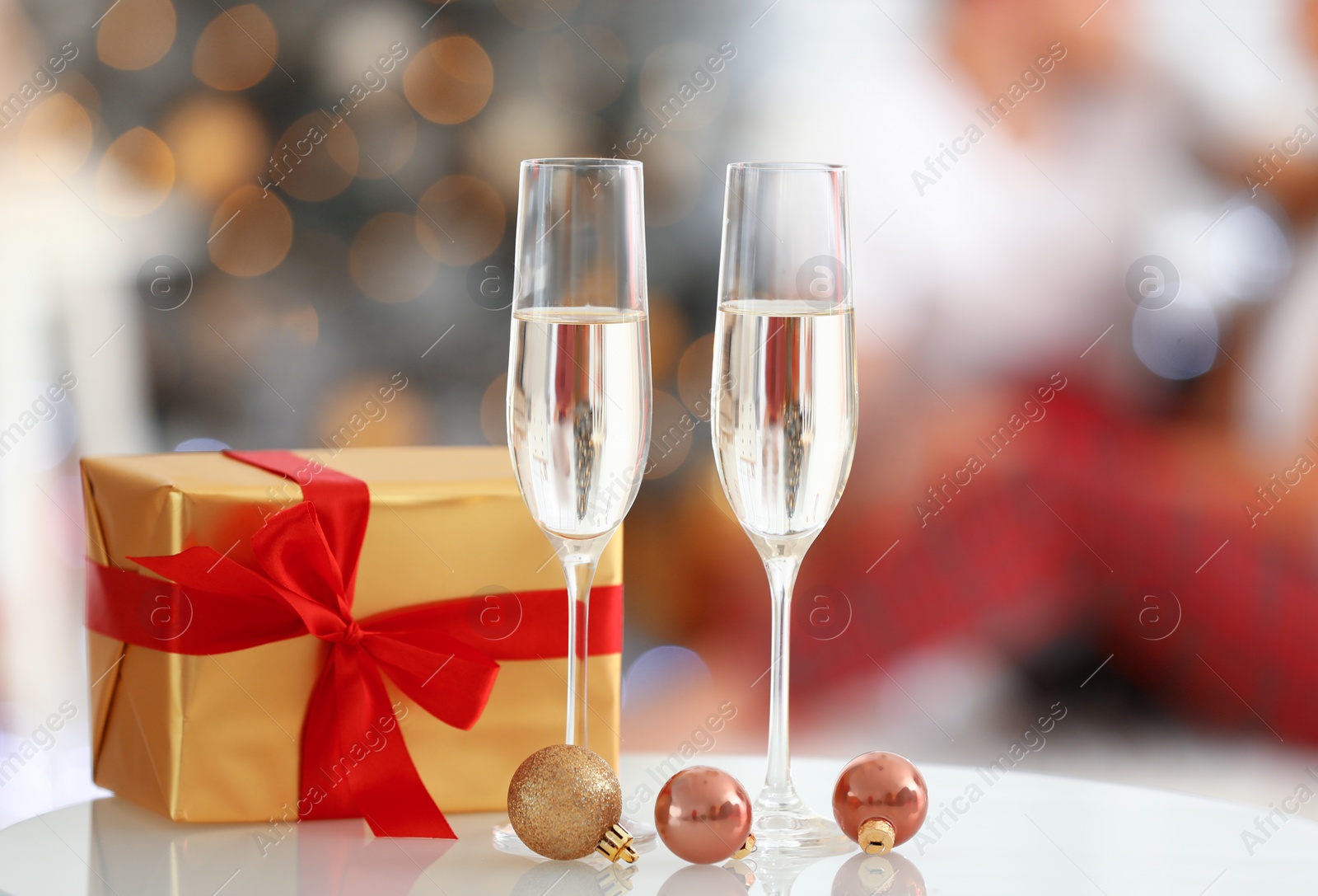 Photo of Christmas gift and glasses of champagne on table against blurred background
