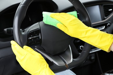 Photo of Woman cleaning steering wheel with rag in car, closeup