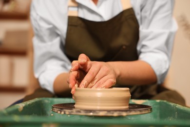 Clay crafting. Woman making bowl on potter's wheel indoors, closeup
