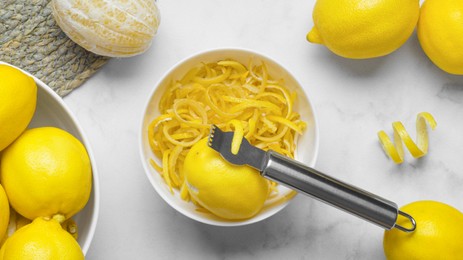 Photo of Bowl with peel pieces, fresh lemons and zester on white marble table, flat lay