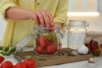 Woman putting tomatoes into pickling jar at kitchen table, closeup