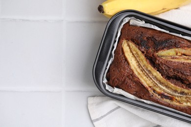 Photo of Delicious banana bread and fresh fruits on white tiled table, top view. Space for text