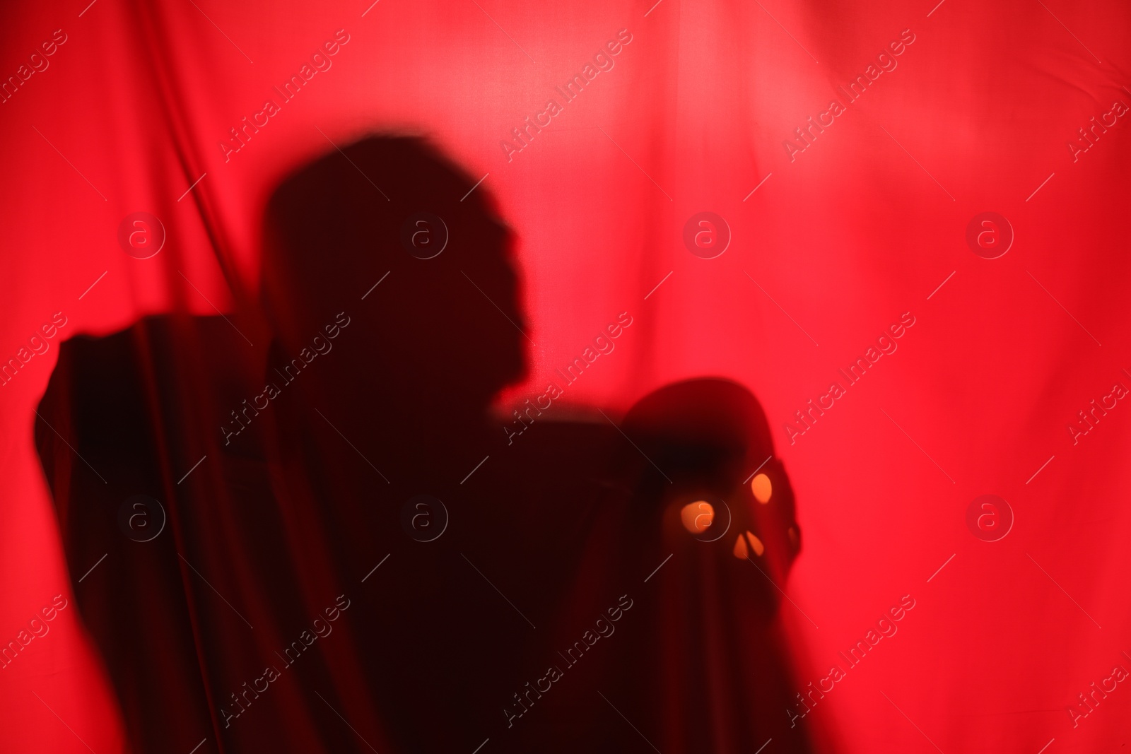 Photo of Silhouette of creepy ghost with skull behind red cloth, space for text