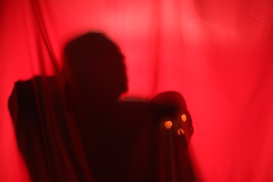 Silhouette of creepy ghost with skull behind red cloth, space for text