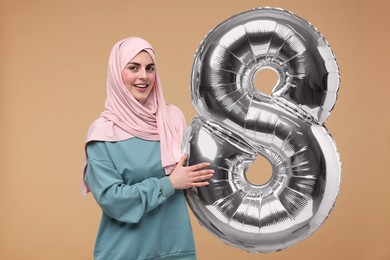 Photo of Happy Women's Day. Woman in hijab with balloon in shape of number 8 on beige background