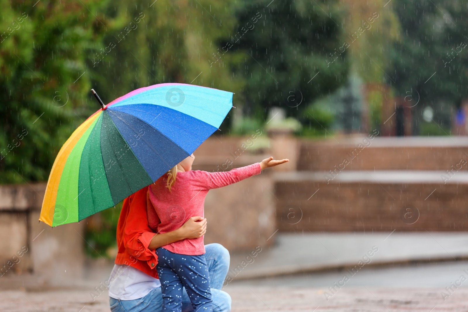 Photo of Mother and daughter with bright umbrella under rain outdoors