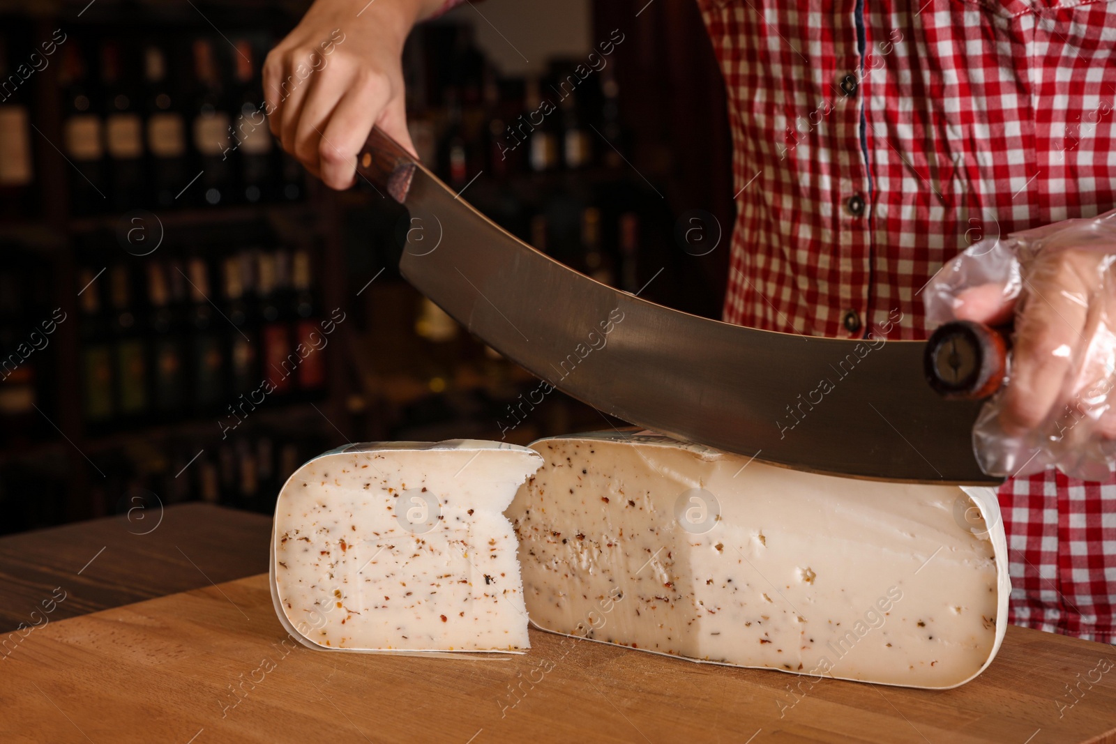 Photo of Seller cutting delicious cheese on table in store