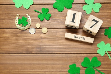 Flat lay composition with clover leaves and block calendar on wooden table, space for text. St. Patrick's Day celebration