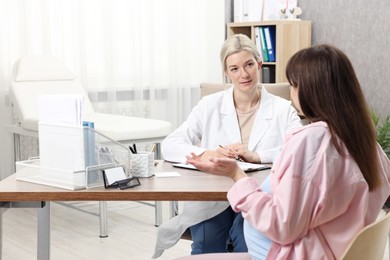 Photo of Doctor consulting pregnant patient at table in clinic