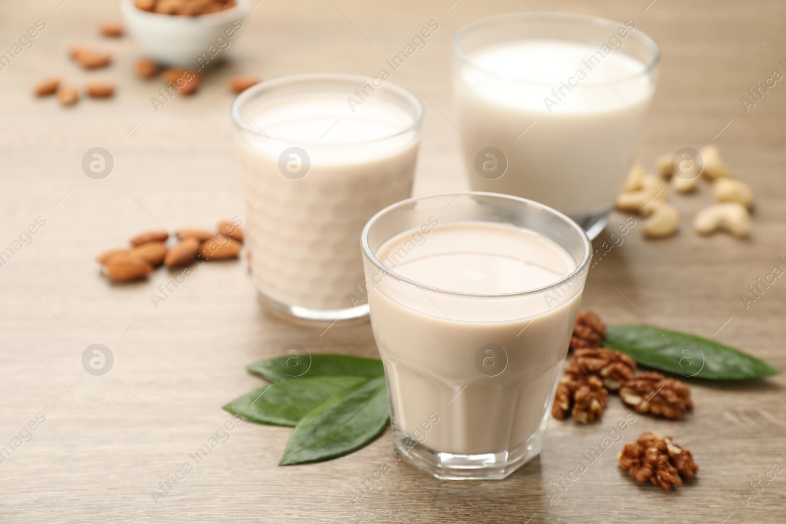 Photo of Different vegan milks and nuts on wooden table, closeup