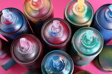 Photo of Many spray paint cans on pink background, above view