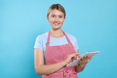 Photo of Beautiful young woman in clean striped apron with tablet on light blue background