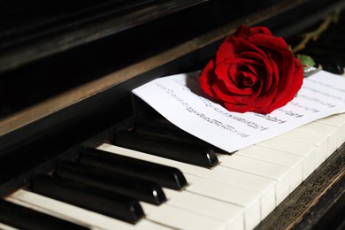 Photo of Beautiful red rose and musical notes on piano keys, closeup