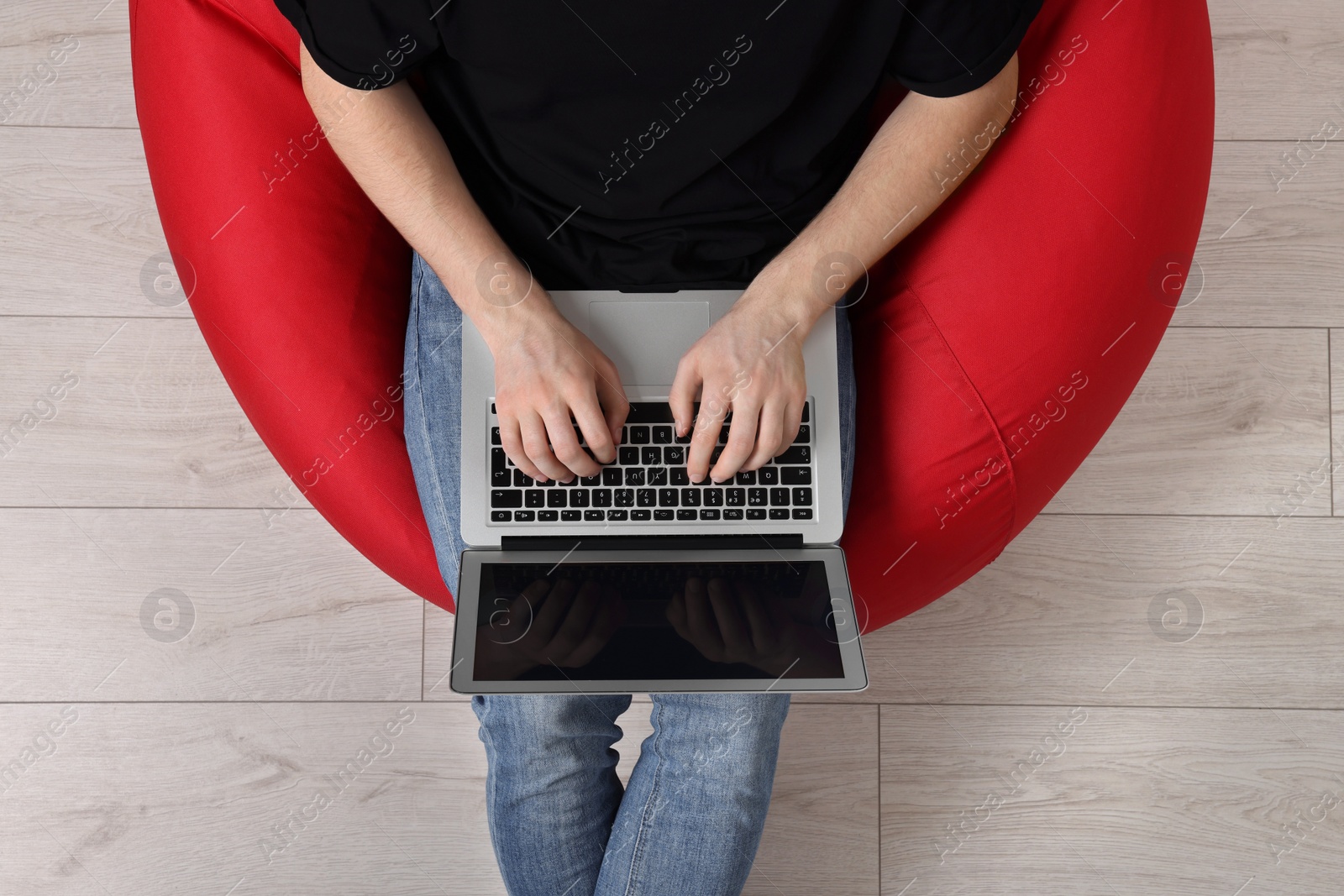 Photo of Man working with laptop in beanbag chair, top view
