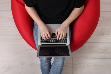 Photo of Man working with laptop in beanbag chair, top view