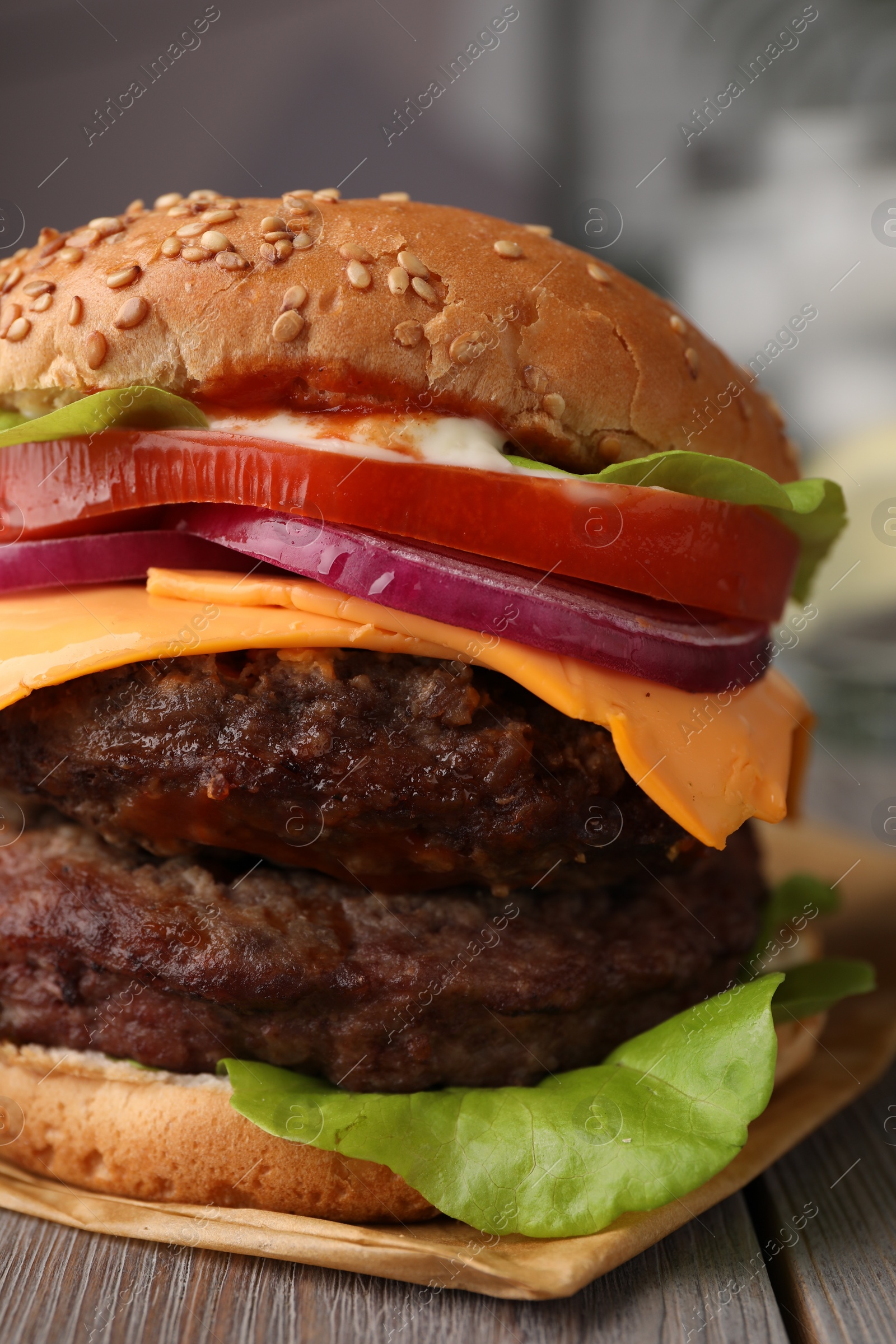 Photo of Tasty cheeseburger with patties on wooden table, closeup