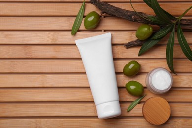 Photo of Tube of natural cream, olives and leaves on wooden table, flat lay. Space for text