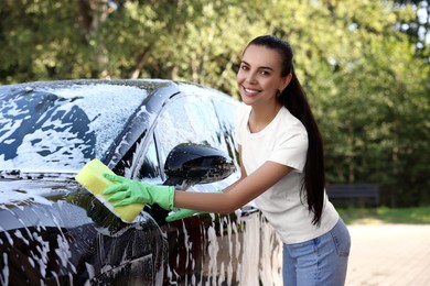 Photo of Happy woman washing car with sponge outdoors