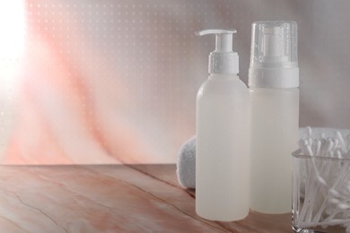 Bottles with face cleansing products and cotton buds on beige marble table. Space for text