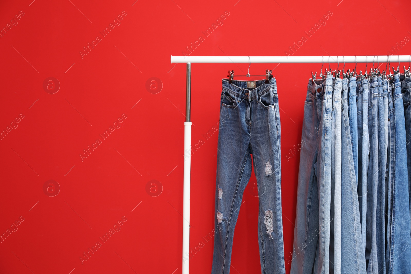 Photo of Rack with stylish jeans on red background. Space for text