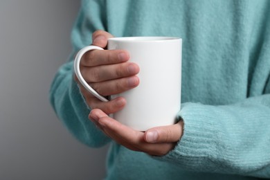 Photo of Woman holding white mug on gray background, closeup