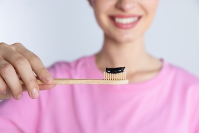 Photo of Woman holding brush with charcoal toothpaste on light background, closeup