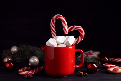 Photo of Cup of tasty cocoa with marshmallows, candy canes and Christmas decor on black wooden table