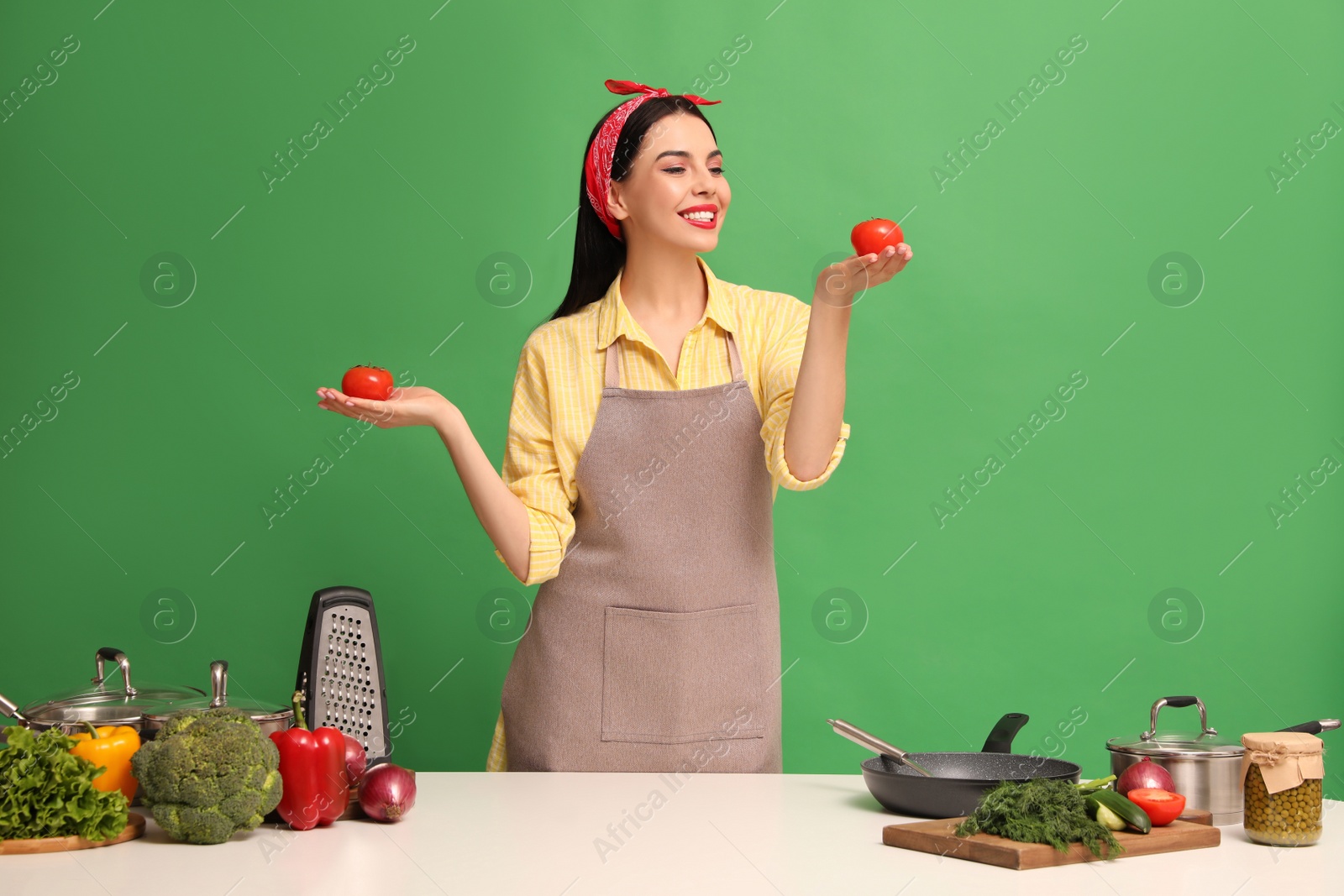 Photo of Young housewife with vegetables and different utensils on green background