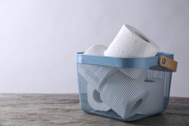Photo of Toilet paper rolls in basket on textured table near light grey wall, space for text