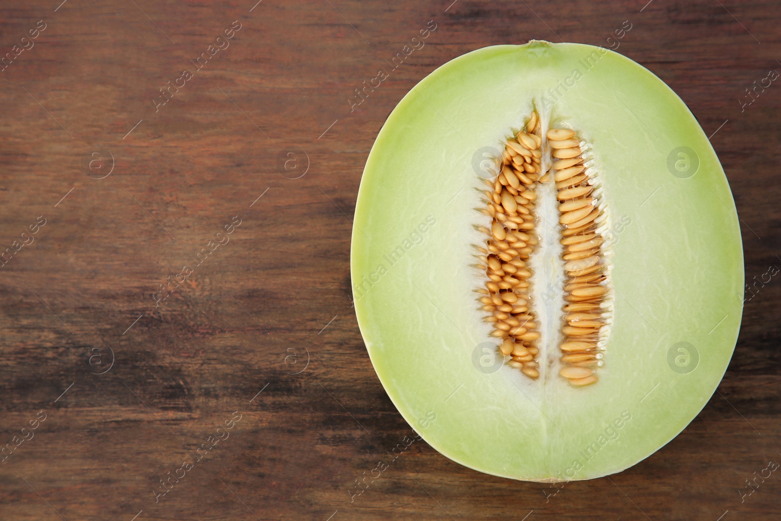 Photo of Half of tasty ripe melon on wooden table, top view. Space for text