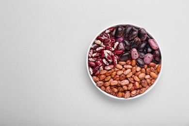 Photo of Different kinds of kidney beans in bowl on white background, top view. Space for text