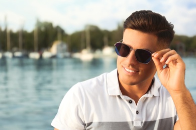 Handsome man wearing stylish sunglasses near river. Space for text
