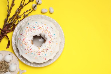 Photo of Easter cake with sprinkles, painted eggs and willow branches on yellow background, flat lay. Space for text