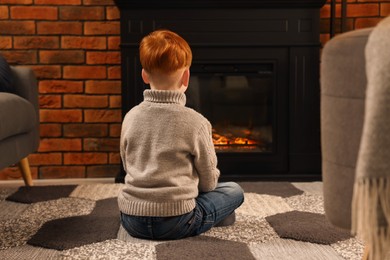 Photo of Boy siting on floor near fireplace at home, back view