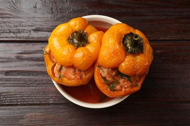 Photo of Tasty stuffed peppers in bowl on wooden table, top view