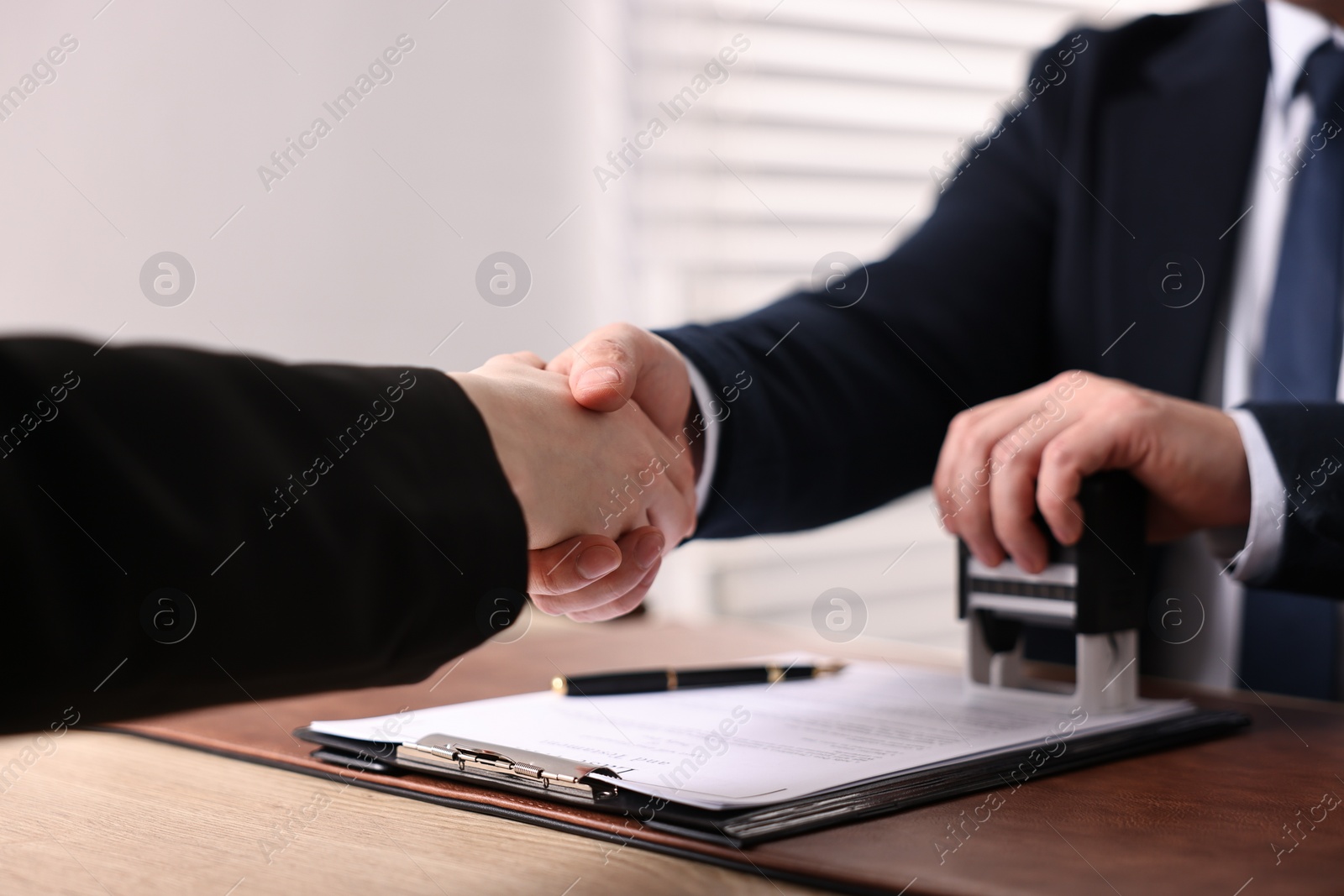 Photo of Notary shaking hands with client at wooden table in office, closeup