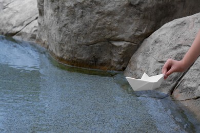 Photo of Kid launching small white paper boat on water outdoors, closeup. Space for text