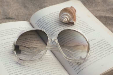 Photo of Beautiful sunglasses, book and shell on sand, closeup