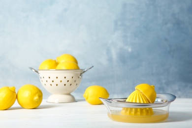 Photo of Ripe lemons and juicer on light table against color background