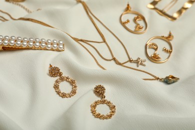 Photo of Stylish golden bijouterie on white fabric. Elegant jewelry