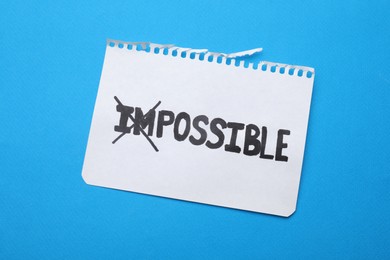 Photo of Motivation concept. Paper with changed word from Impossible into Possible by crossing over letters I and M on light blue background, top view