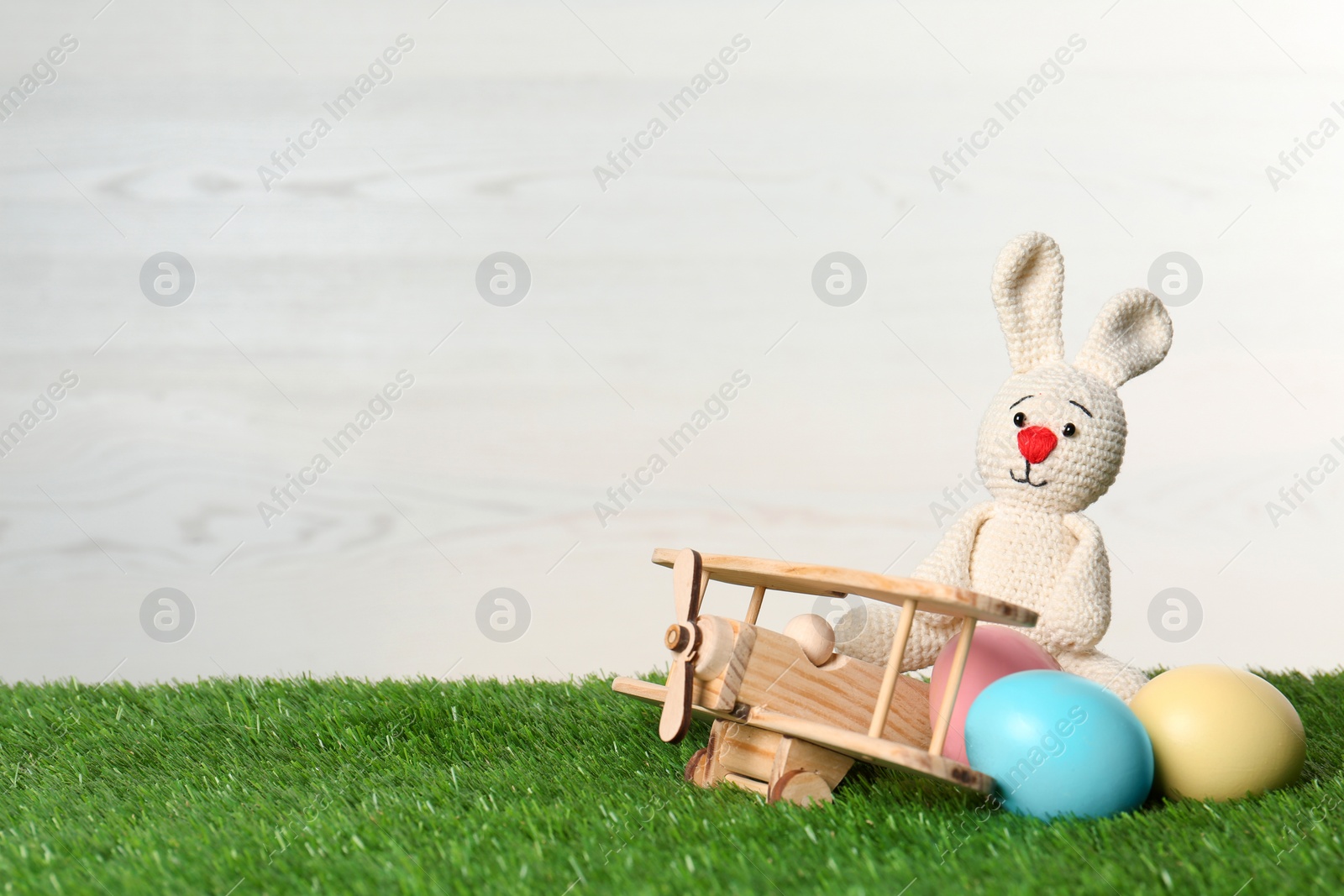 Photo of Wooden airplane with cute Easter bunny toy and dyed eggs on green grass, space for text