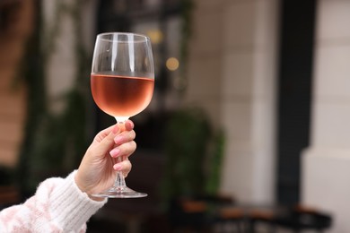 Photo of Woman holding glass of rose wine outdoors, closeup. Space for text